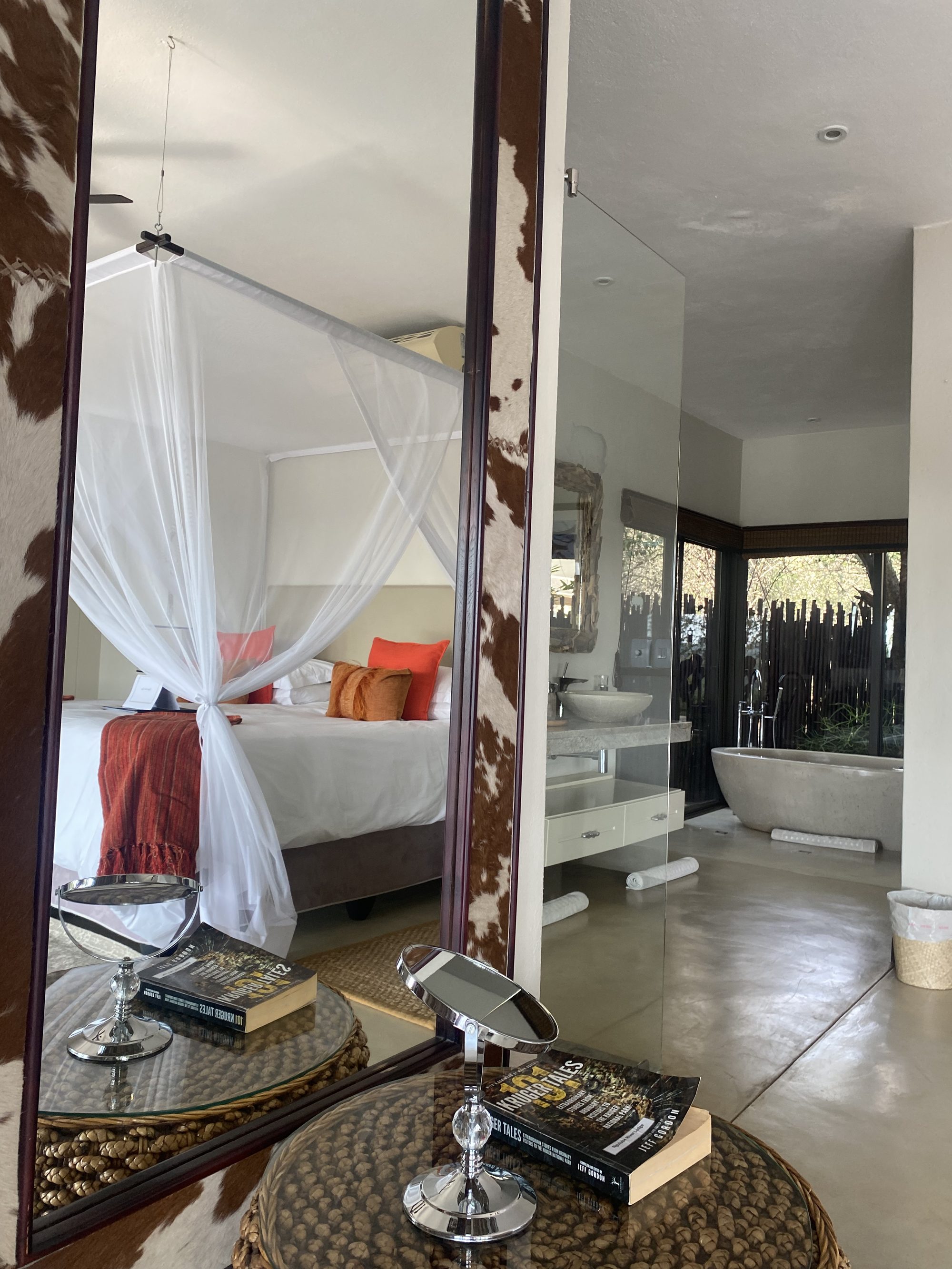 A suite bedroom reflected in a cowhide mirror, with the bath beyond
